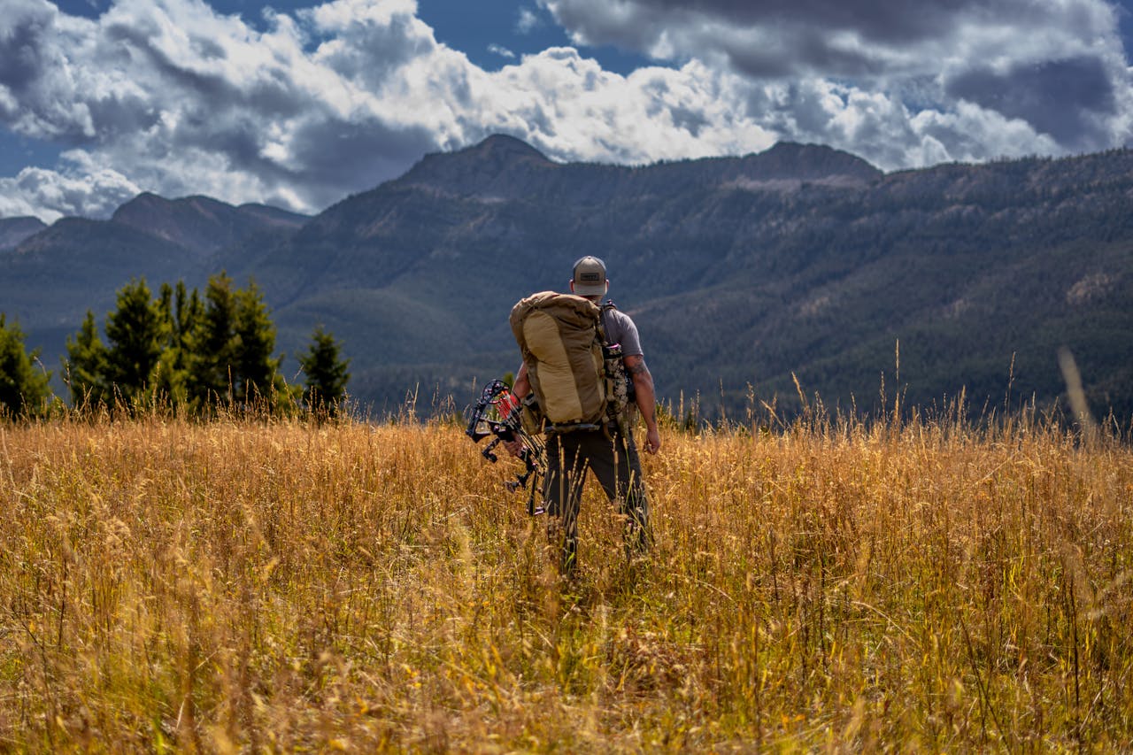 Man with backpack trekking through a mountainous pasture under dramatic skies.